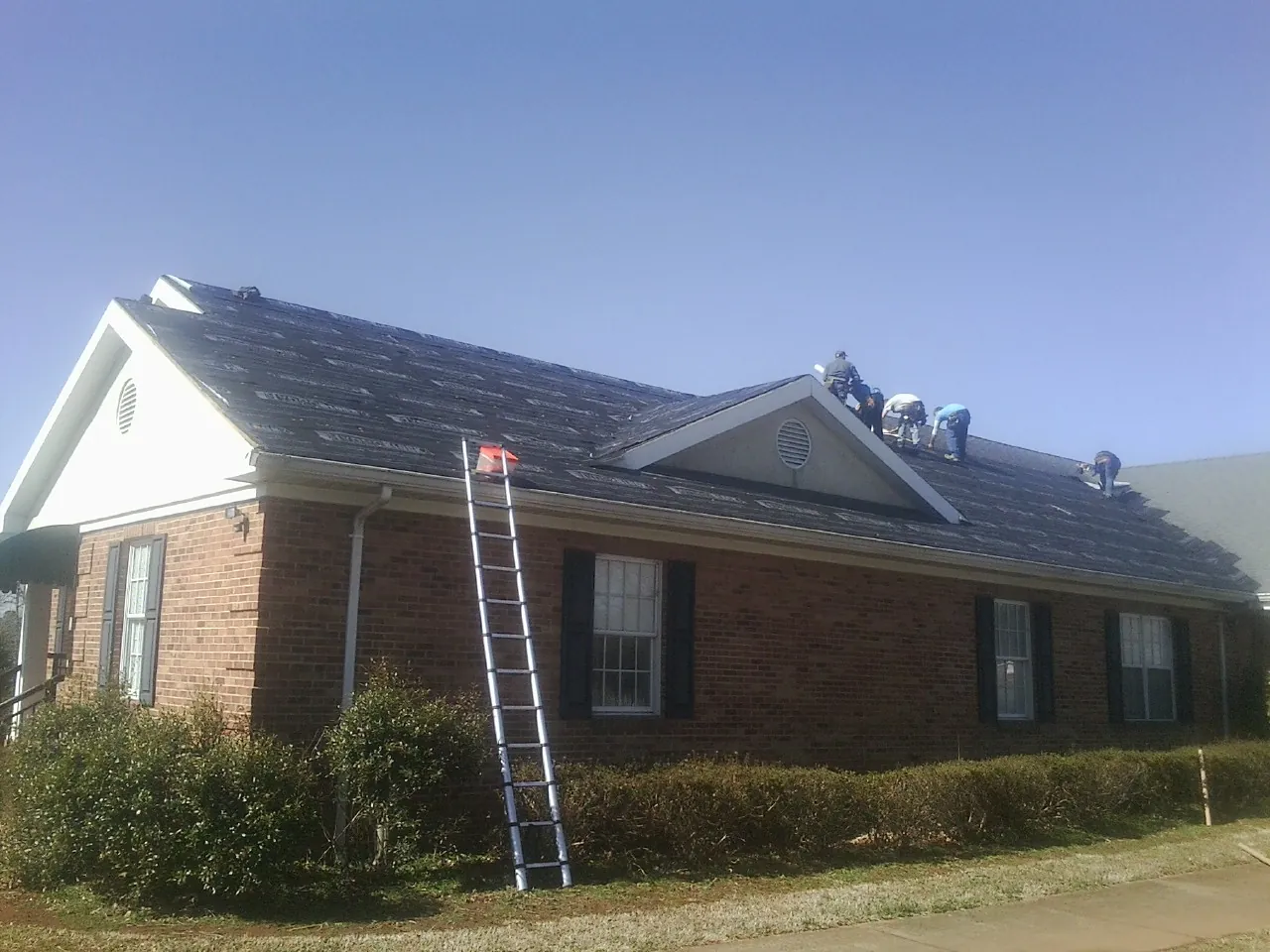 Crew tearing shingles off a brick ranch roof with a ladder set — Emergency Roof Repair work by our crew in Harwood