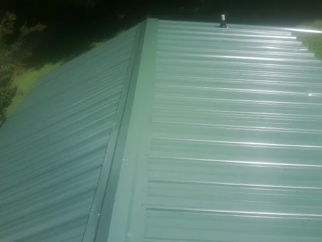 New green metal panels meeting at the ridge of a roof — Flat Roof Repair work by our crew in Harwood