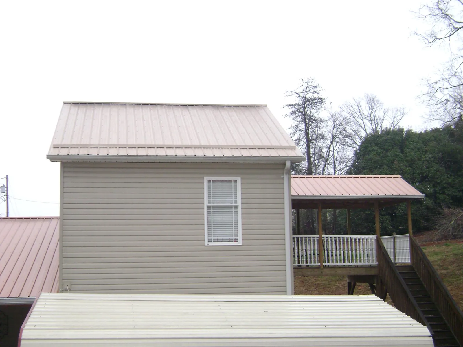Tan metal roofs on a two story addition and attached porch, from a Roof Replacement job in Harwood